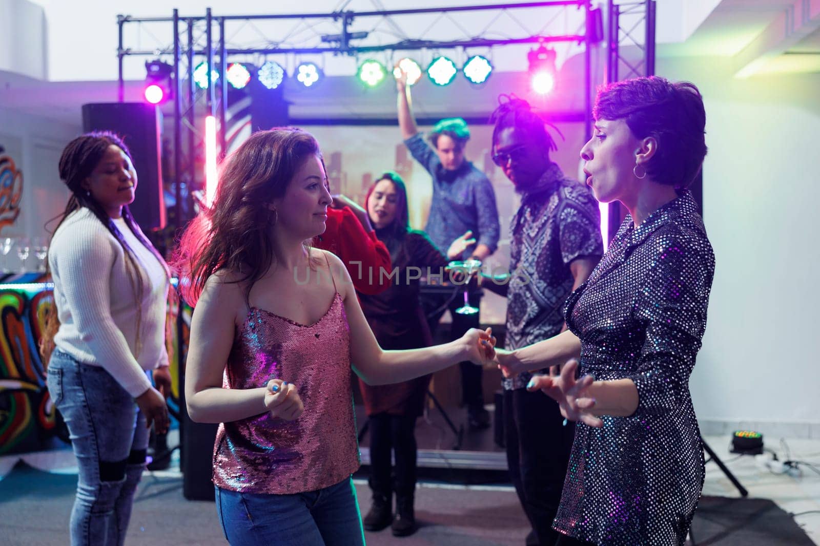 Carefree women dancing in crowded nightclub at live music concert. Cheerful young girlfriends partying with friends and dancing at clubbers gathering event during dj performance