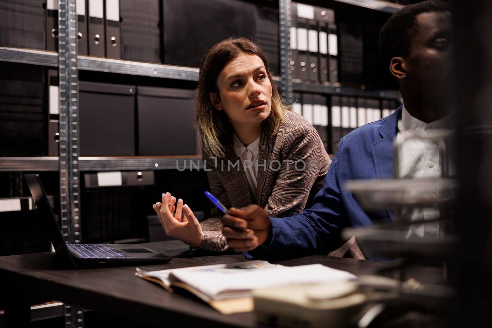 Diverse team reading accountancy report, working overhours at management research in storage room. Businesspeople analyzing administrative files, searching for bureaucracy record.