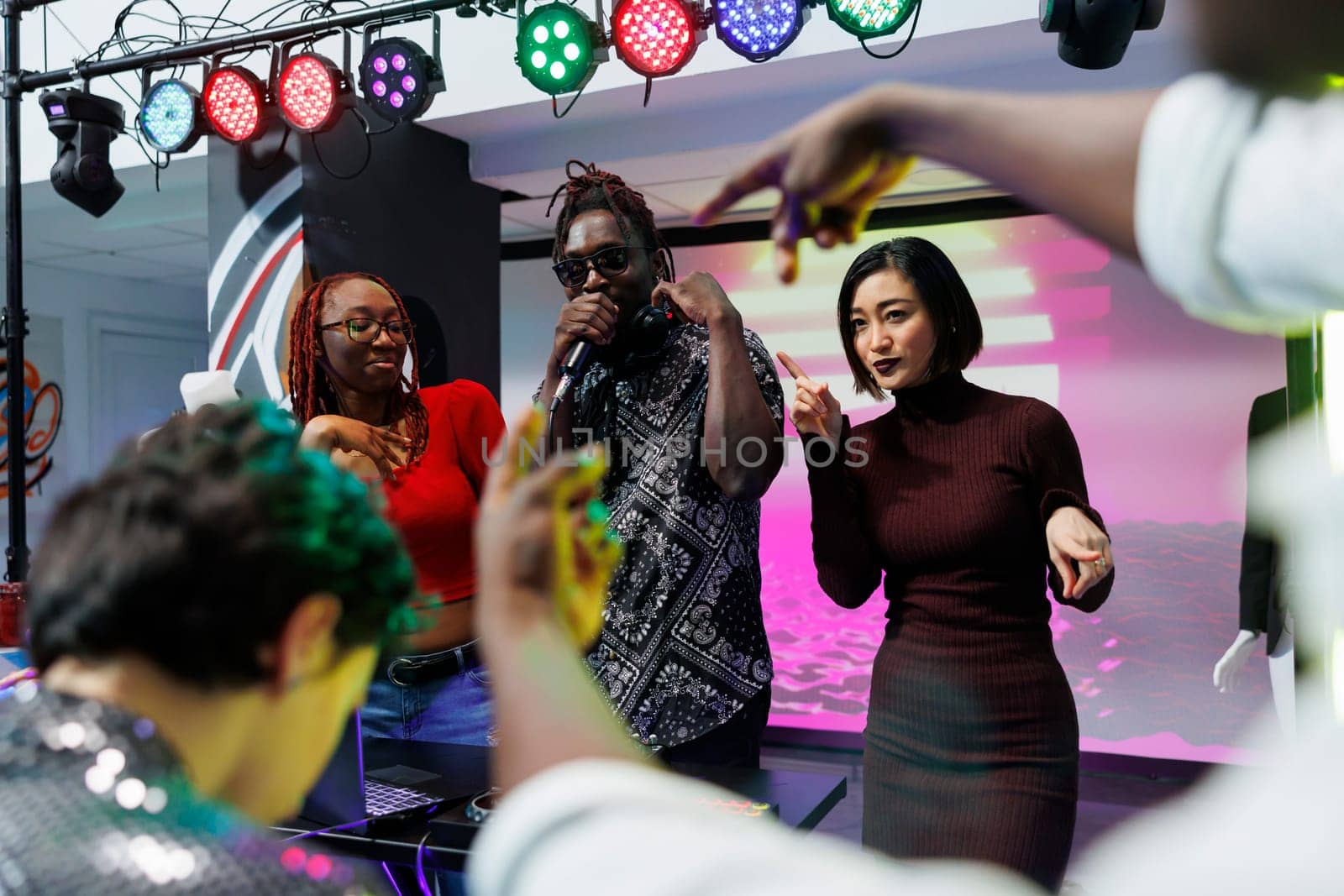 African american musician singing in microphone at electronic music festival live concert in nightclub. Diverse man and women partying and performing on stage at event in club