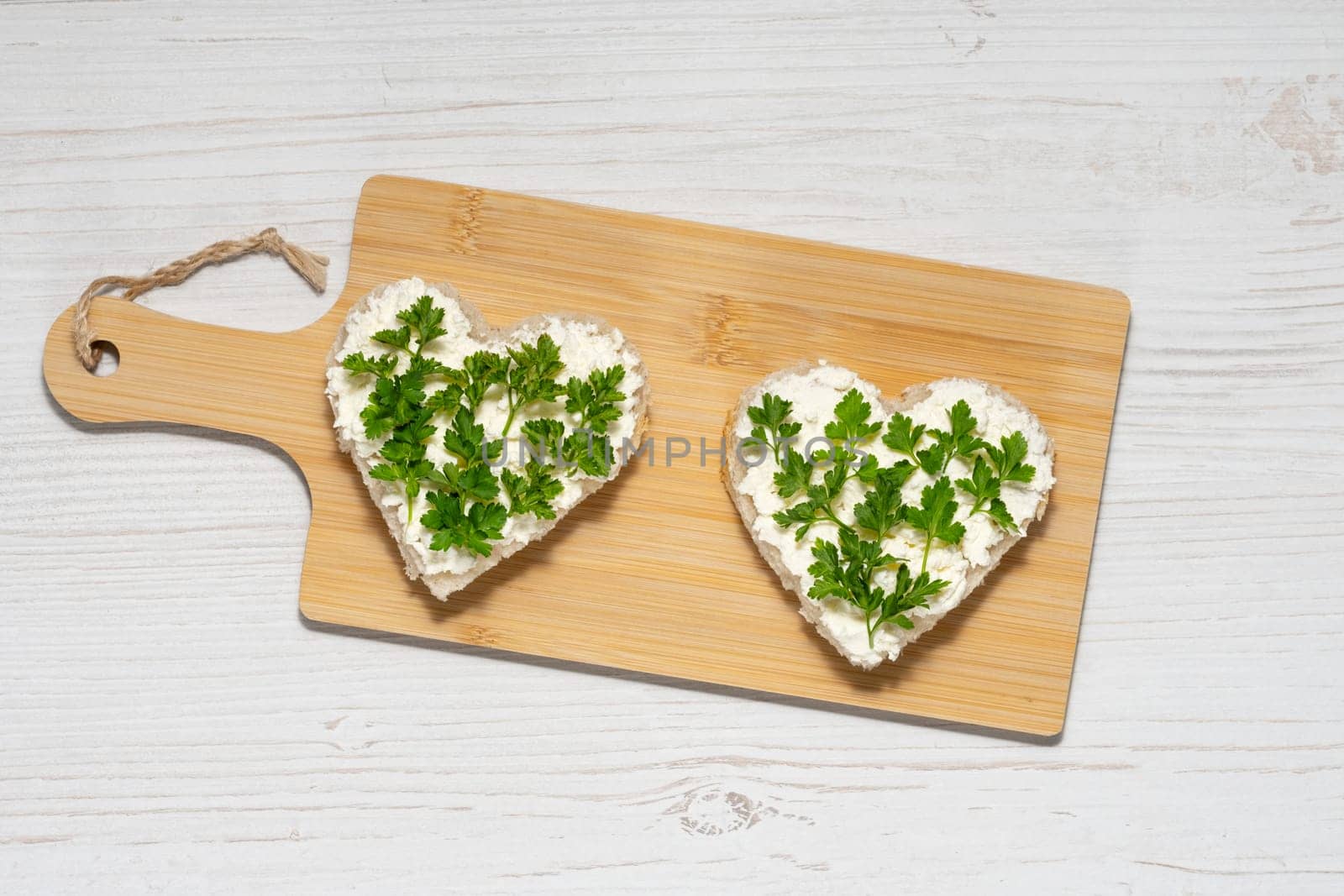 Two heart-shaped sandwiches with cottage cheese and parsley.
