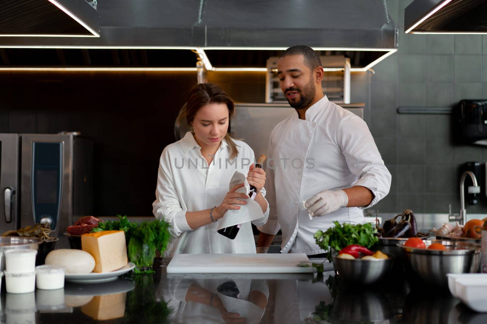 Black chef is cooking with woman on kitchen using red wine as an ingredient.. African american chef teaches a girl how to cook. Man and woman cooking in professional kitchen.