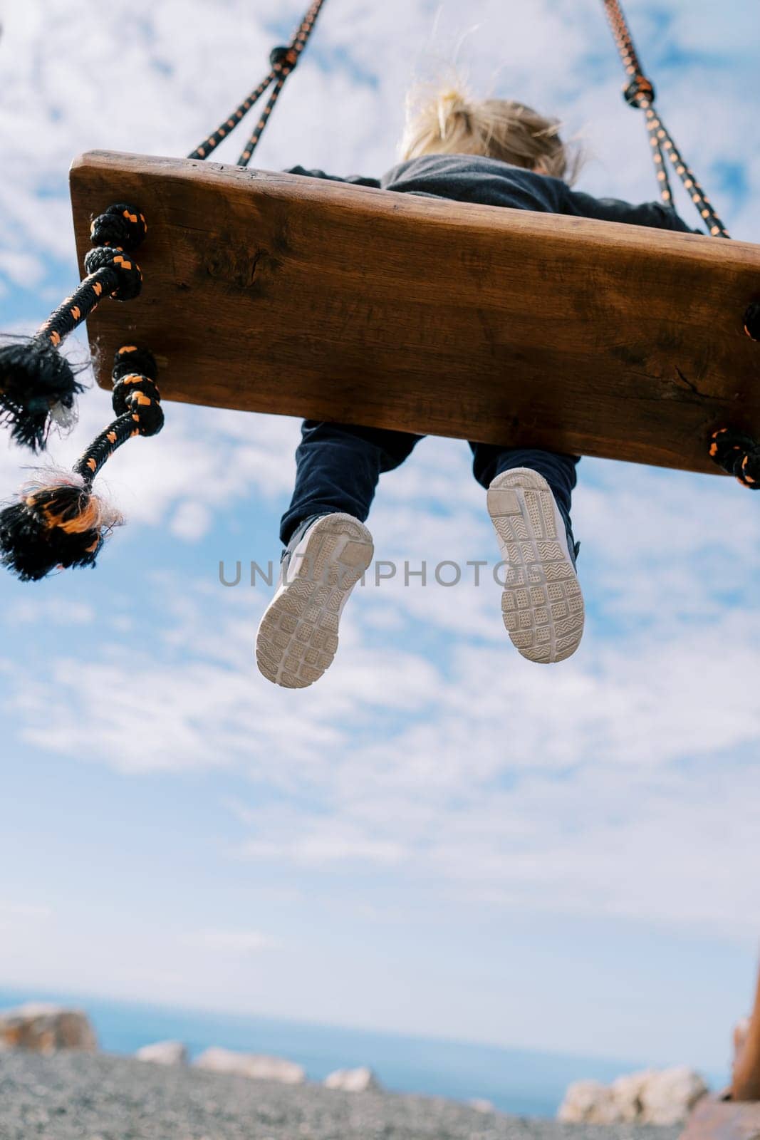 Little girl swings on a rope swing on the seashore against the sky. Bottom view. High quality photo