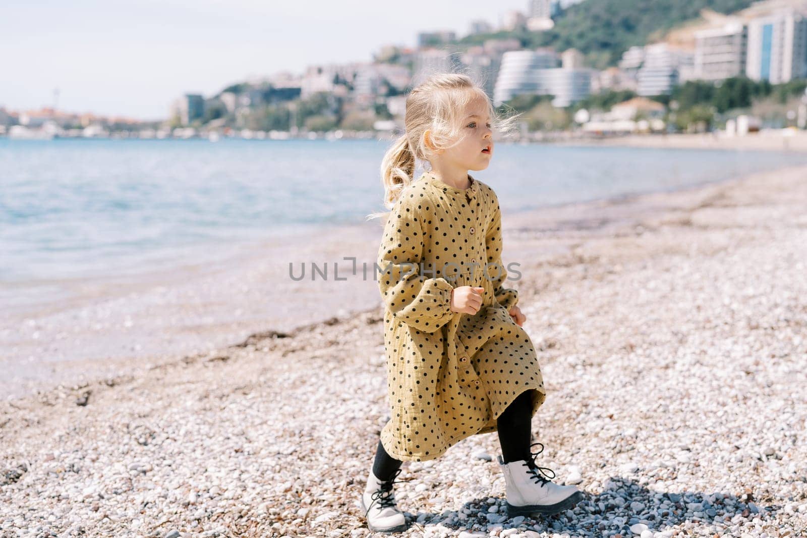 Little girl walks along a pebble beach and looks away. High quality photo