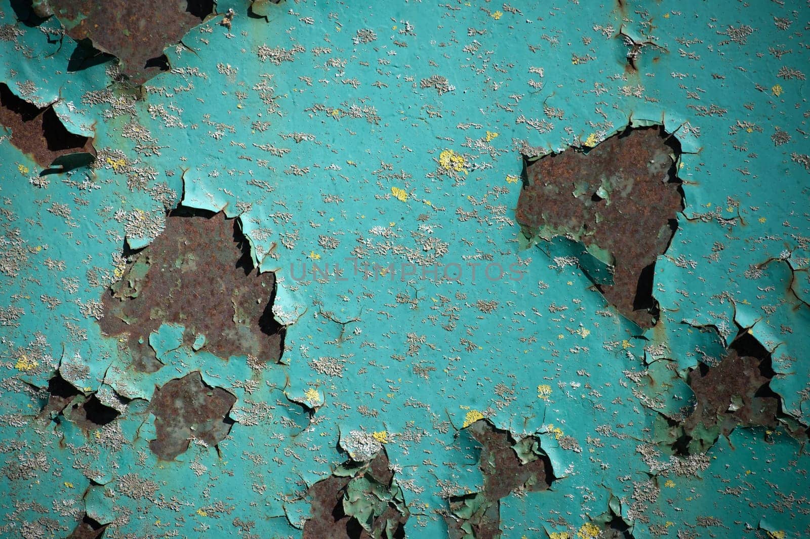 Turquoise paint chips and peels away, it reveals the darker rusted metal beneath, contrasting the once vibrant paint with the corroded surface