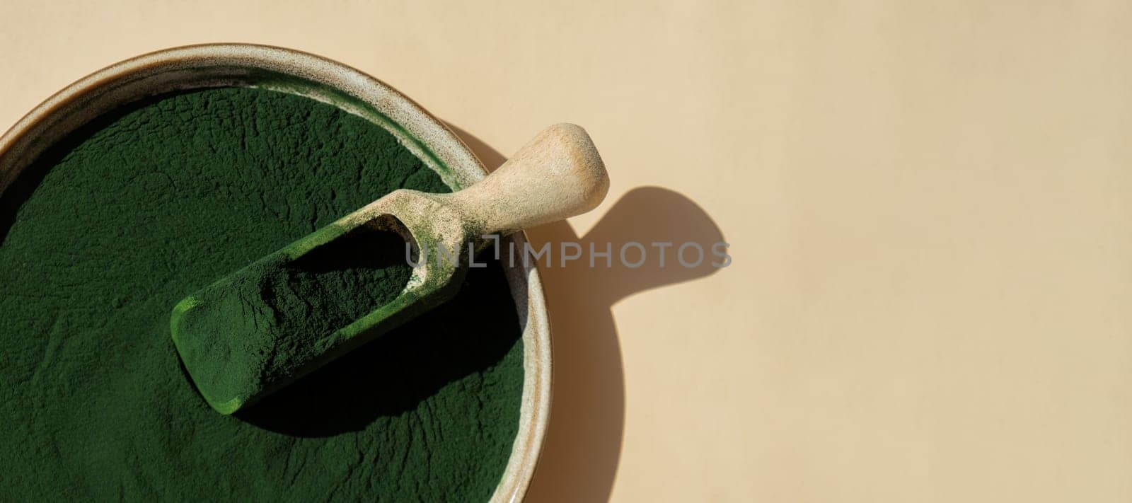 Natural organic green spirulina algae powder in bowl and wooden spoon on neutral background. Chlorella seaweed vegan superfood supplement source and detox. Copy space Healthy nutritional antioxidant concept