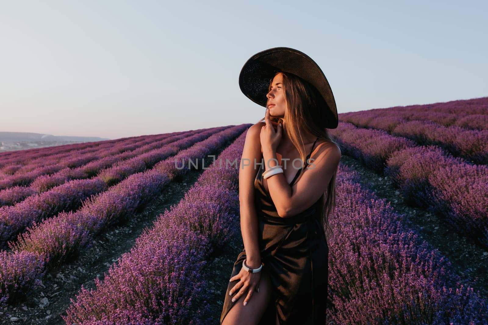 Woman lavender field. Happy carefree woman in black dress and hat with large brim walking in a lavender field during sunset. Perfect for inspirational and warm concepts in travel and wanderlust. by panophotograph