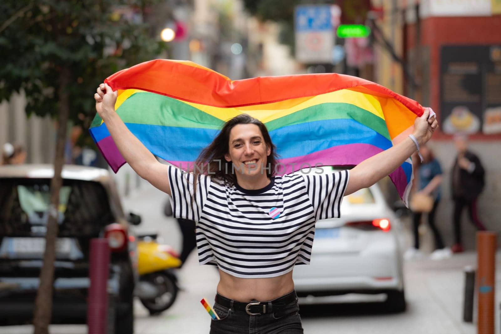 Portrait of a happy transgender girl waving a rainbow flag in a city street. LGBTQ community and diversity concept by papatonic