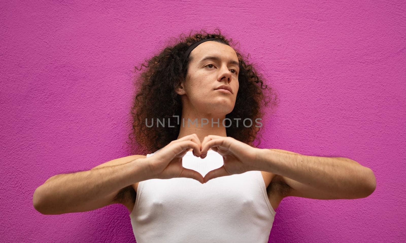 Studio shot of a gay man doing heart symbol shape with hands isolated on purple background.