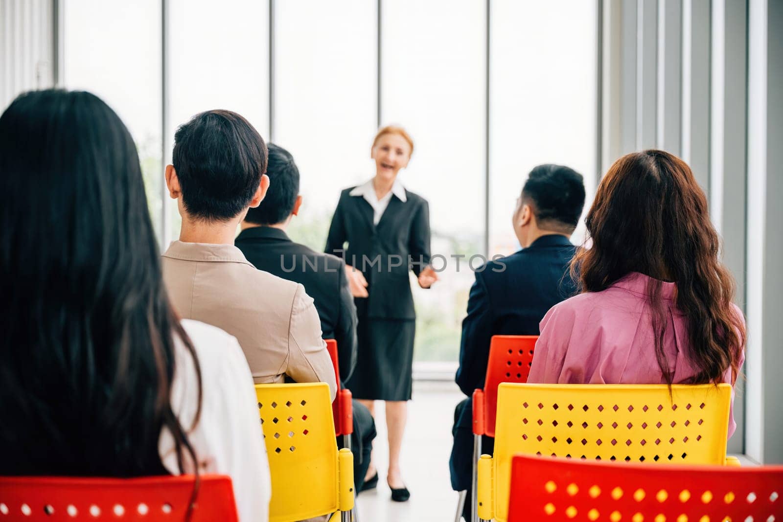 A confident senior corporate coach, experienced and wise leads a seminar for business team. female director and CEO engage with employees in office meeting, actively discussing projects and guiding.