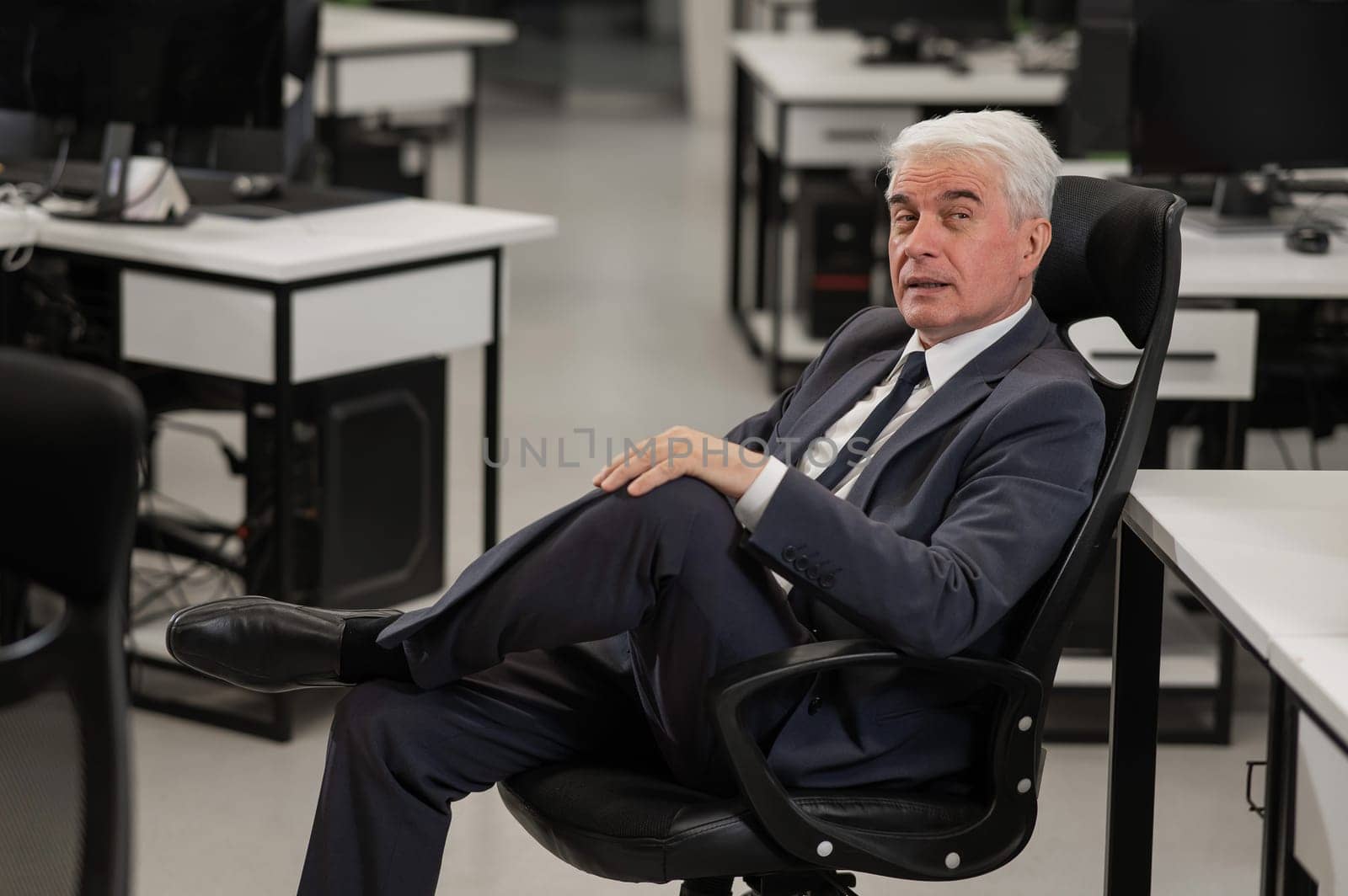Portrait of a pensive mature business man sitting in a chair in the office. Vertical photo. by mrwed54