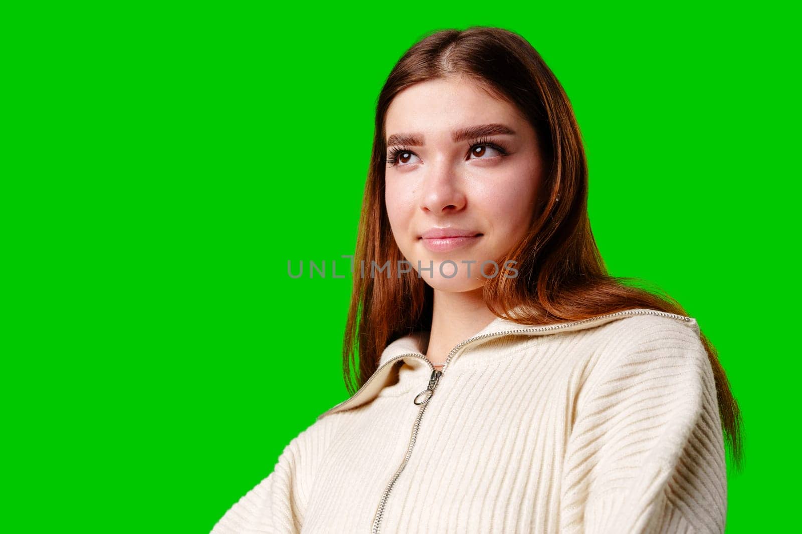 A young woman stands confidently against a vivid green background, dressed in a casual yet fashionable white cropped hoodie and a gray pleated skirt. Her expression is serene with a hint of contemplation, and her body language exudes a relaxed poise.