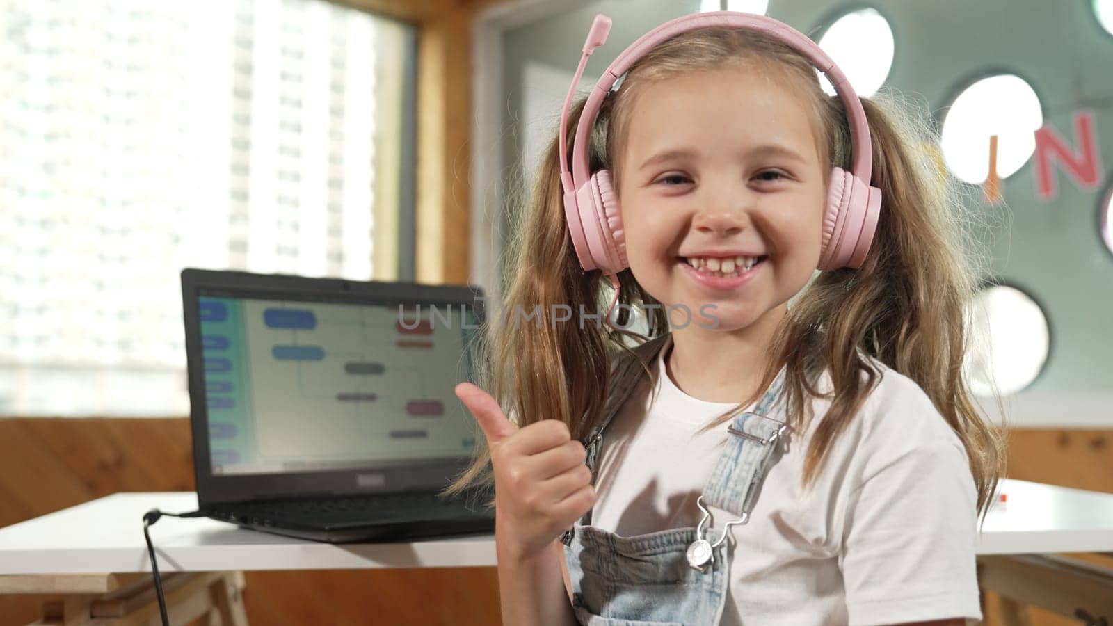 Closeup of caucasian girl smiling to camera while showing a thumb up gesture. Young child wearing headphone and casual dress standing while looking at camera with satisfy, happy, joyful. Erudition.
