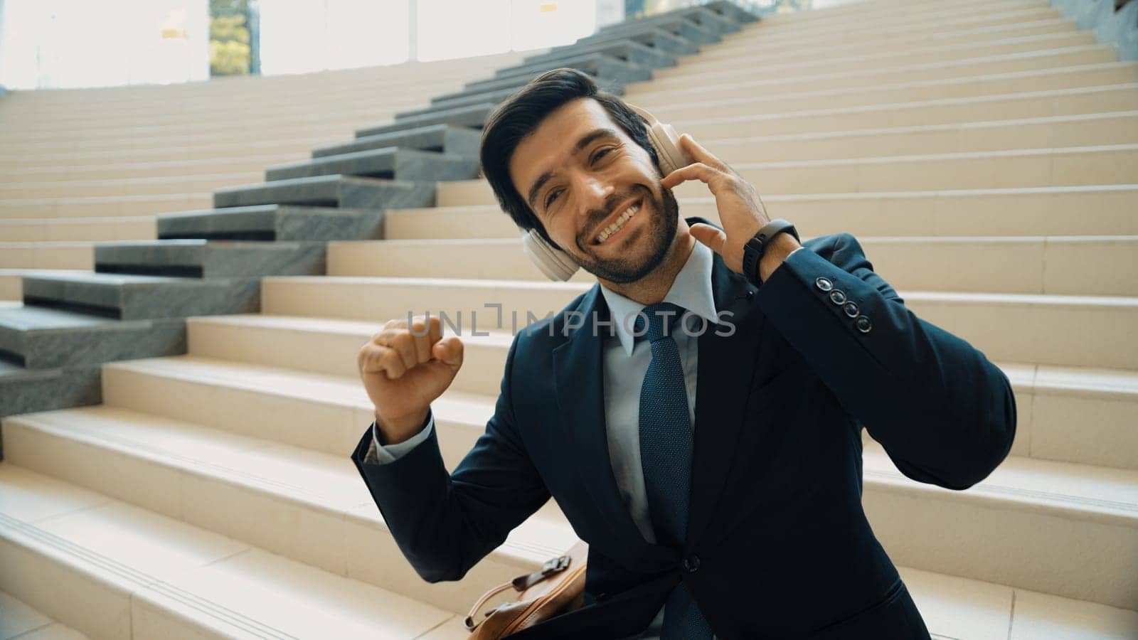 Closeup image of professional business man enjoy to listen music by using headphone. Portrait of skilled project manager show facial expression about joy and happy while sitting at mall. Exultant.