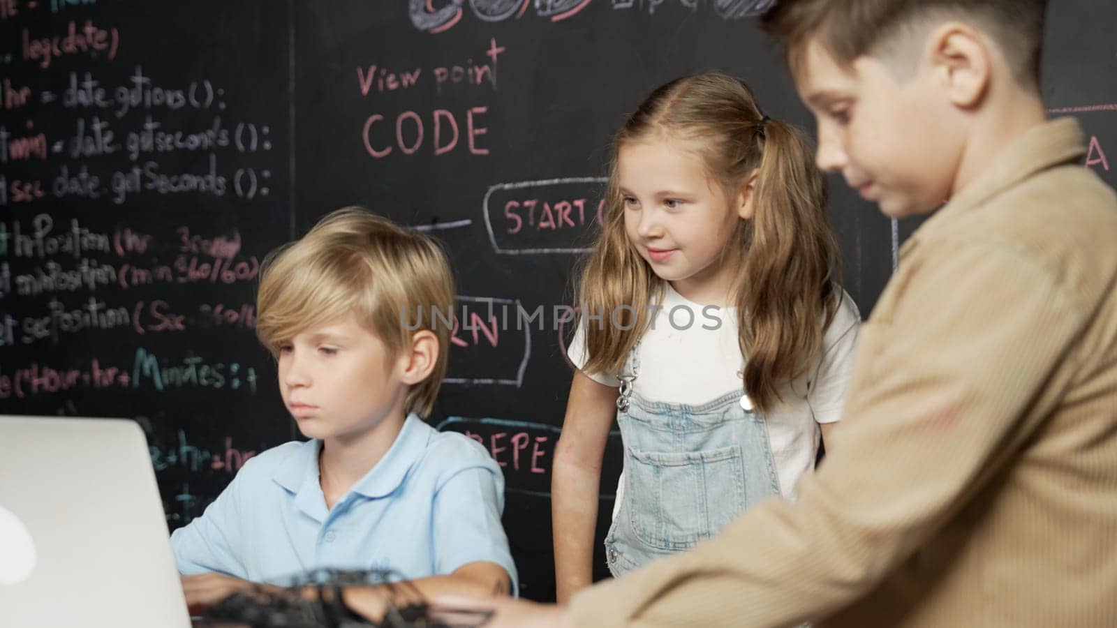 Closeup of boy using laptop programing engineering code and writing program while group of smart diverse student standing surrounded by friend in STEM technology classroom at blackboard. Erudition.