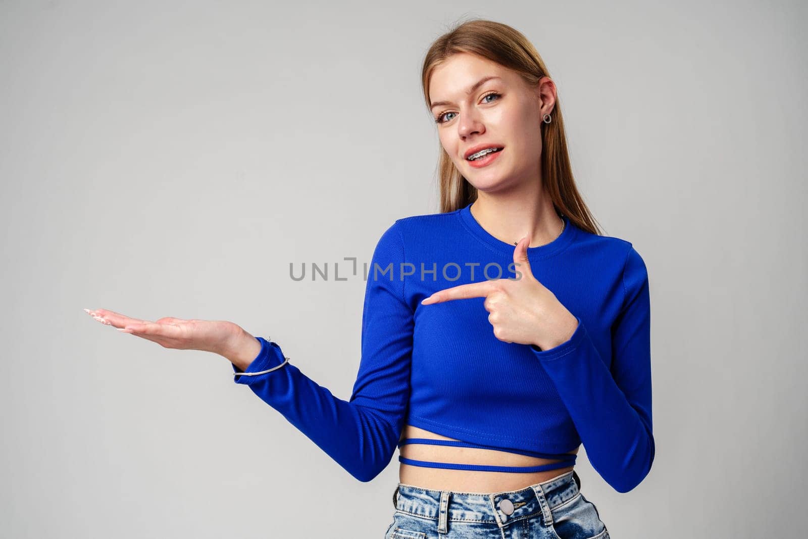 Woman in Blue Top Pointing With Hand Against Neutral Background in studio