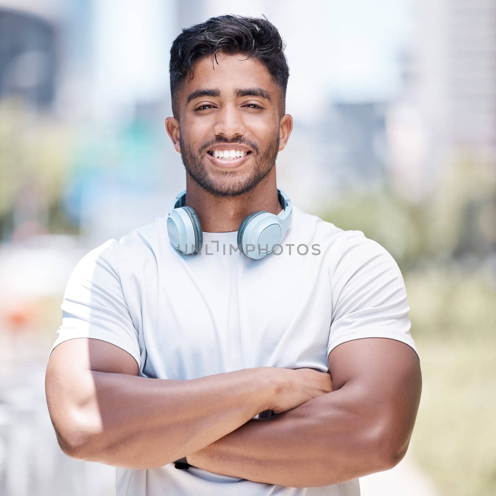 Man, arms crossed in portrait and headphone outdoor for fitness, music or audio streaming with personal trainer in city. Confident, proud and athlete with wireless tech for radio, podcast or playlist by YuriArcurs