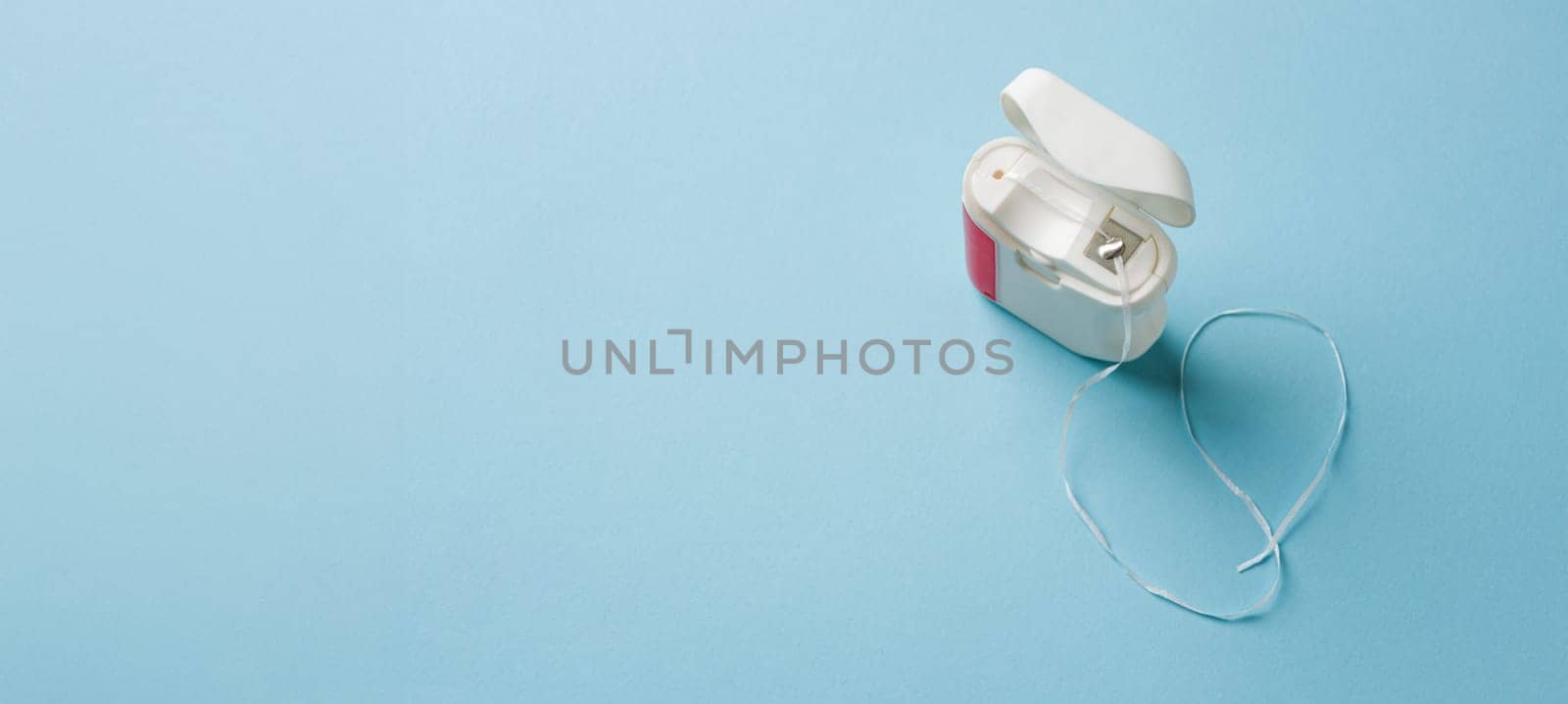 Top view of dental floss in white box on blue background by Sonat