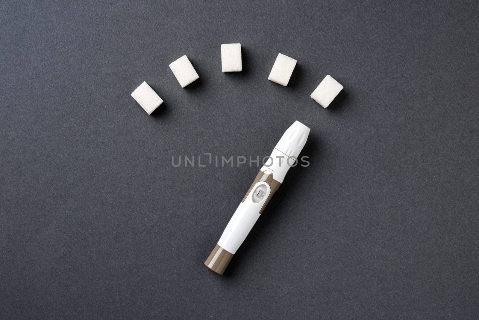 Blood sugar level displayed with sugar cubes and a lancet pen on a dark background by Sonat