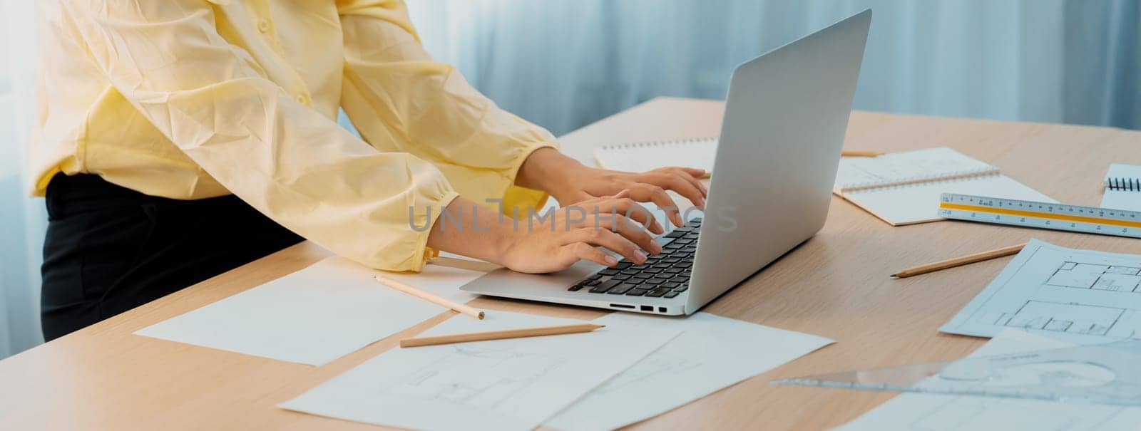 Professional architect working on laptop at modern office on working table with architectural equipment and blueprint scatter around. Living and design concept. Focus on hand. Closeup. Delineation.