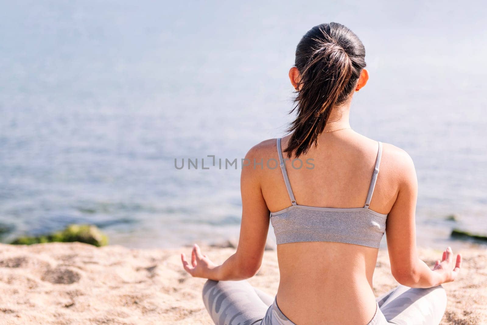 rear view of a young woman meditating at beach by raulmelldo