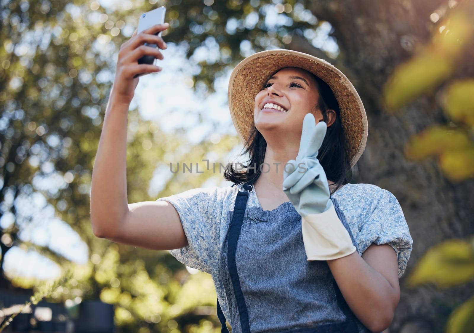 Happy, woman and florist taking selfie with smartphone for social media, networking outdoor in nature at nursery. Excited, female person and peace sign with mobile for connection and entertainment by YuriArcurs