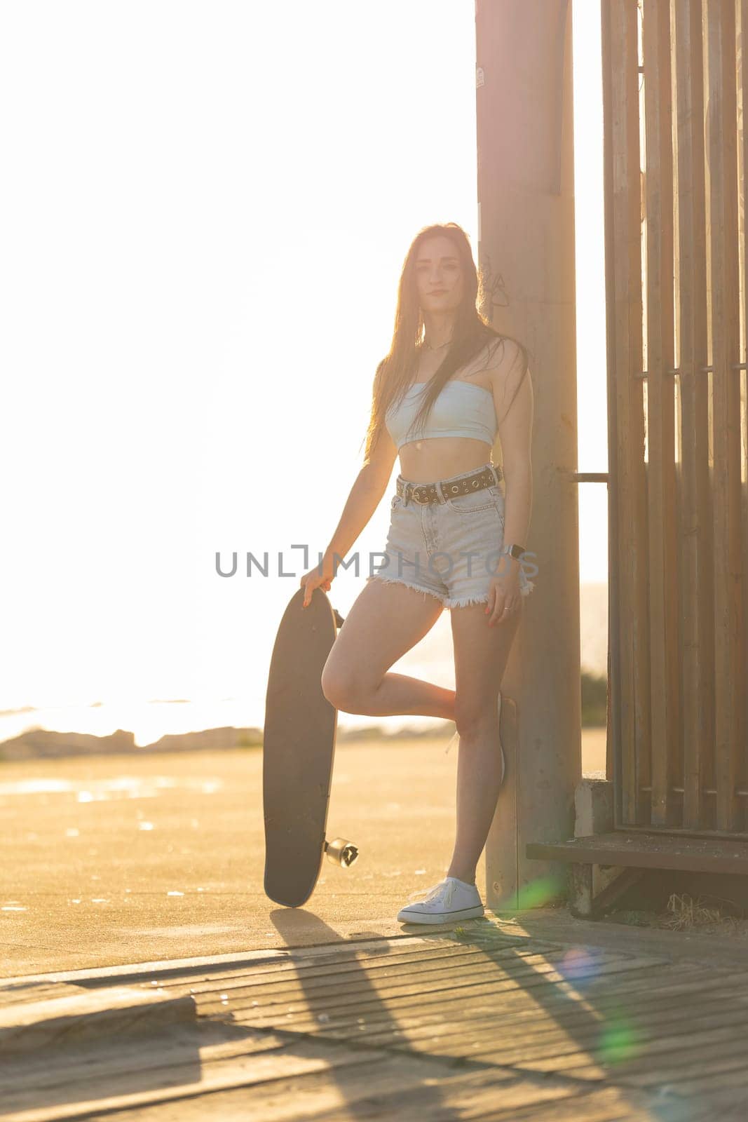 A woman is standing on a beach holding a skateboard. She is wearing shorts and a tank top