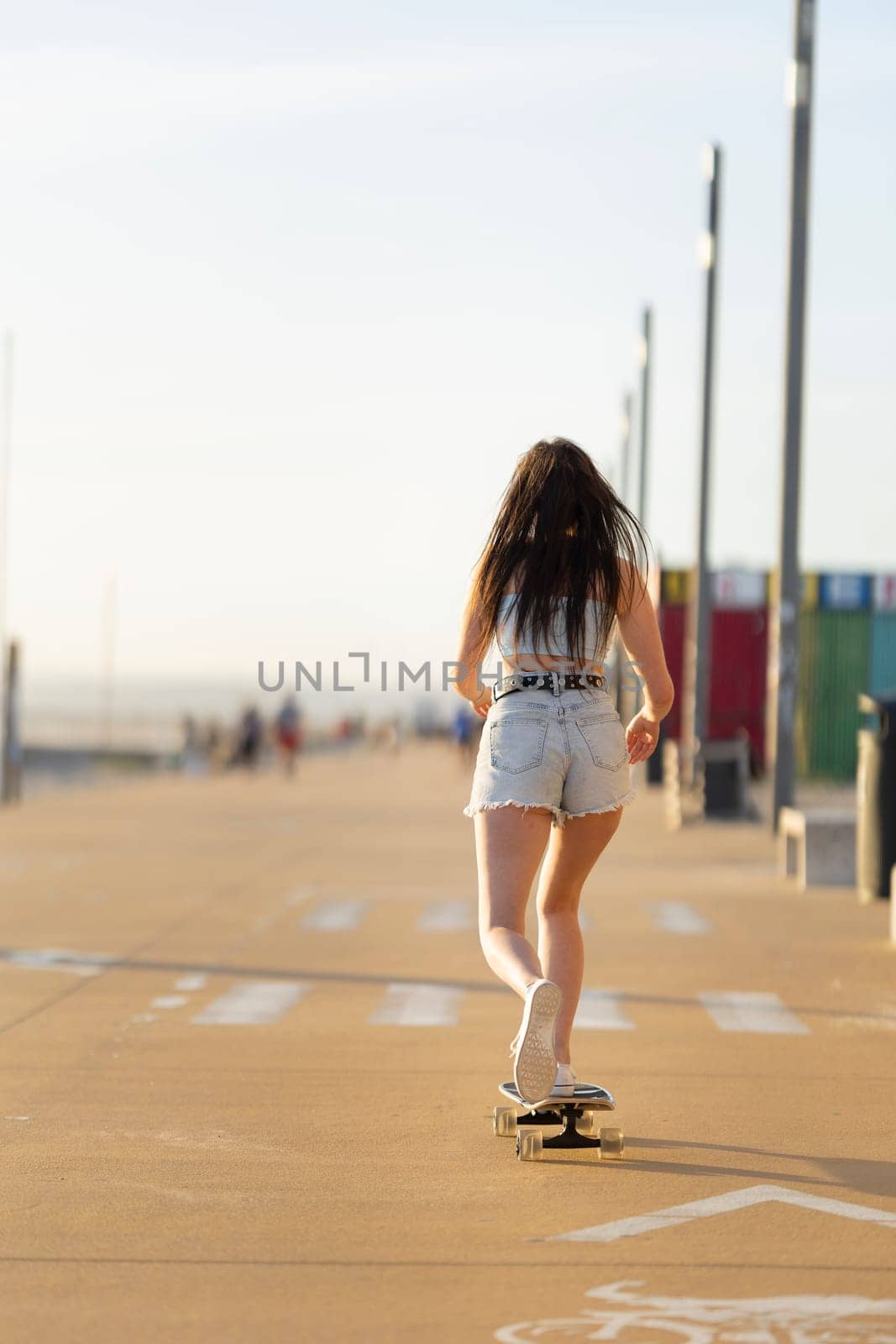 A woman is skateboarding down a sidewalk. She is wearing shorts and a white shirt. The scene is sunny and bright