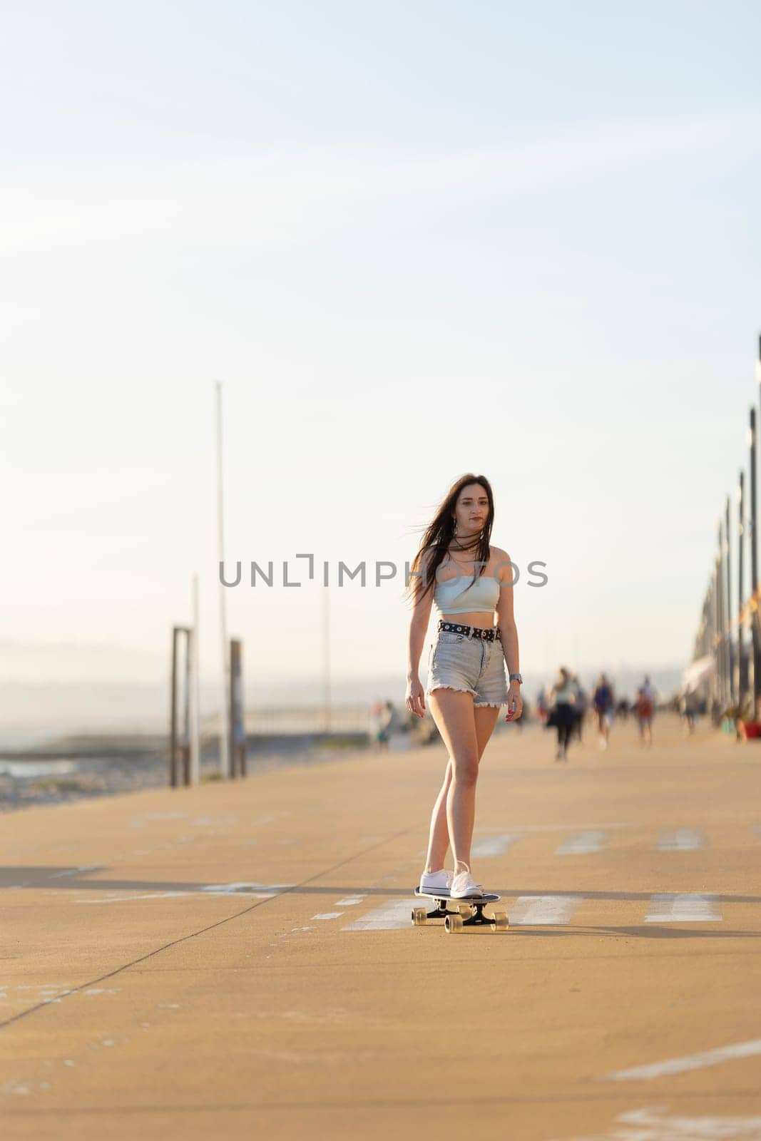 A woman is skateboarding on a sidewalk near the beach by Studia72