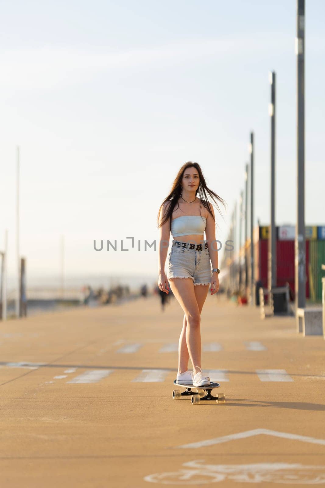 A woman is skateboarding down a street. She is wearing a blue shirt and shorts