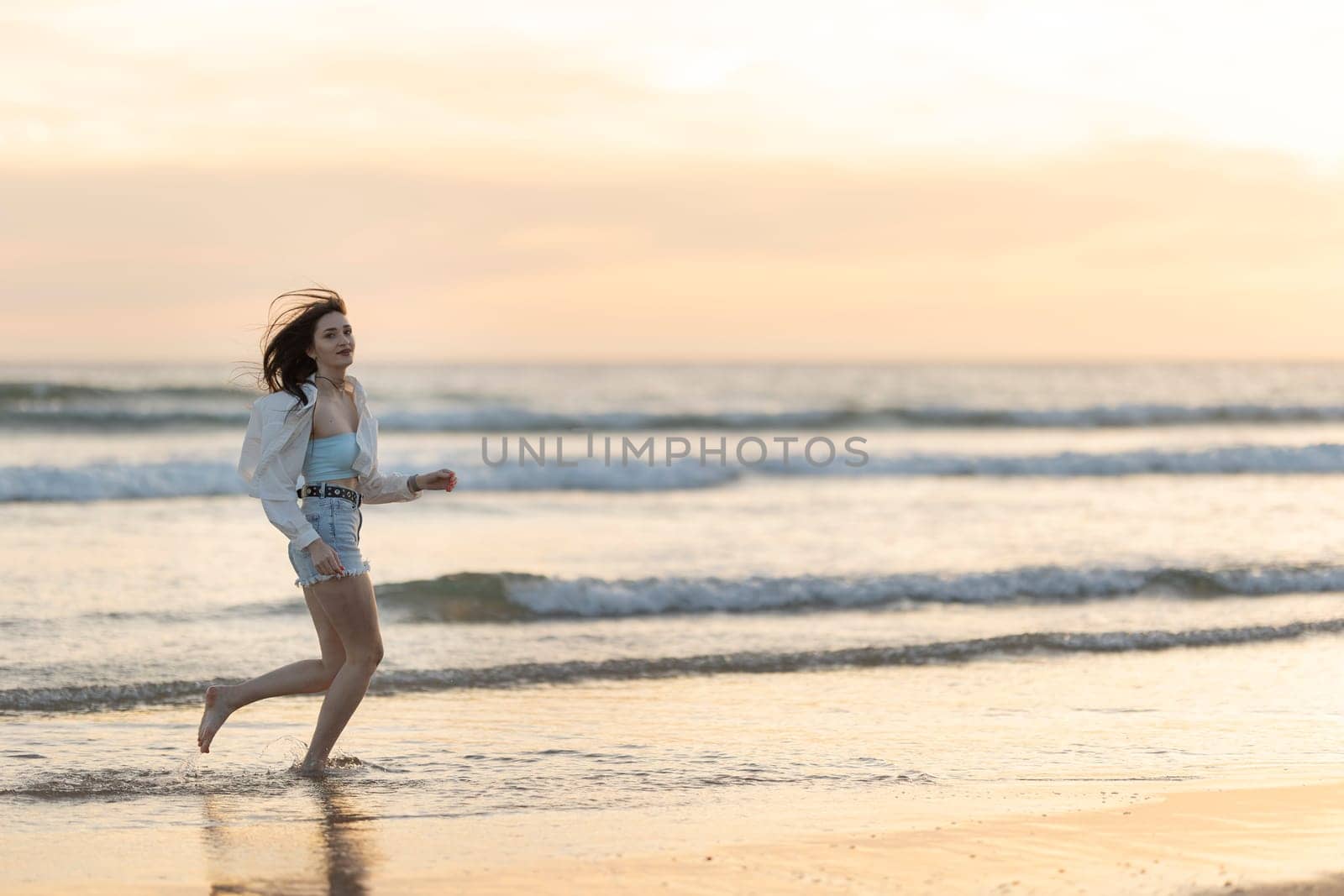 A woman is running on the beach with the sun setting in the background by Studia72