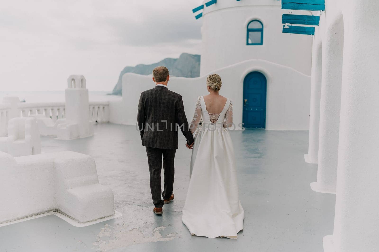 A bride and groom are walking down a path in front of a blue door. The bride is wearing a white dress and the groom is wearing a suit. Scene is romantic and happy. by Matiunina