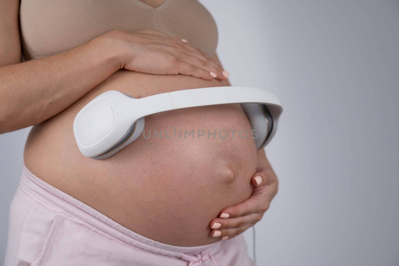 A pregnant woman holds headphones against her bare tummy. The expectant mother lets her child listen to music. by mrwed54