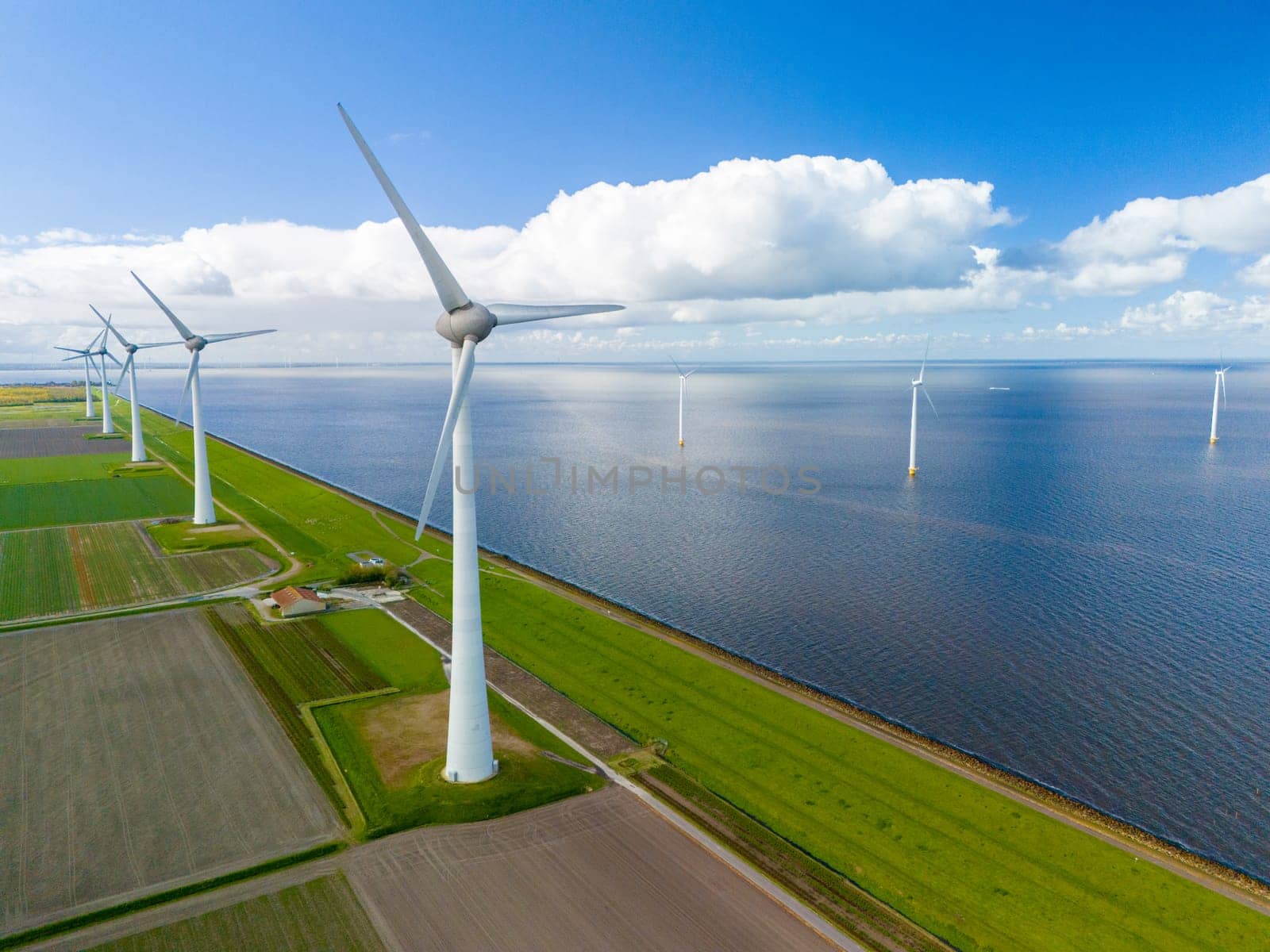 A wind farm generates clean energy in the middle of a vast Dutch lake, with rows of windmill turbines spinning gracefully under the spring sky. Ijsselmeer windmill turbines Noordoostpolder Netherlands