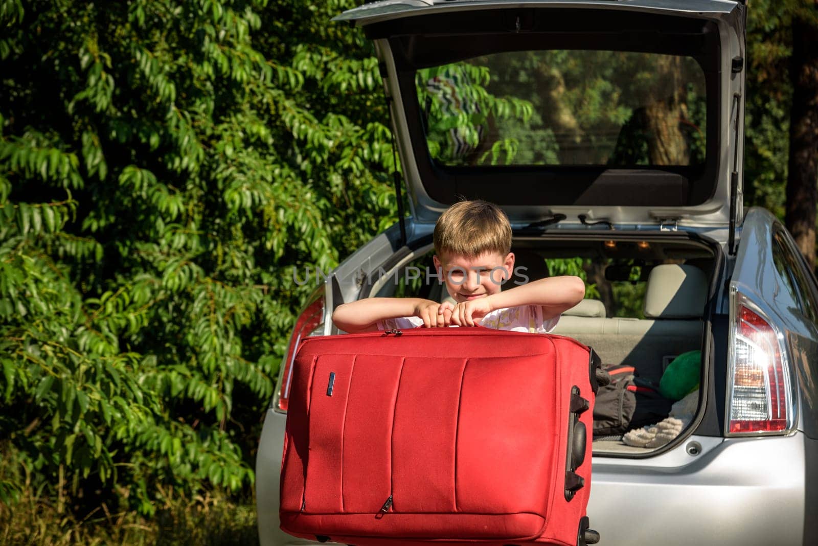 Pretty boy loading the luggage in the trunk of the car. Kid looking forward for a road trip or travel. Family travel by car.