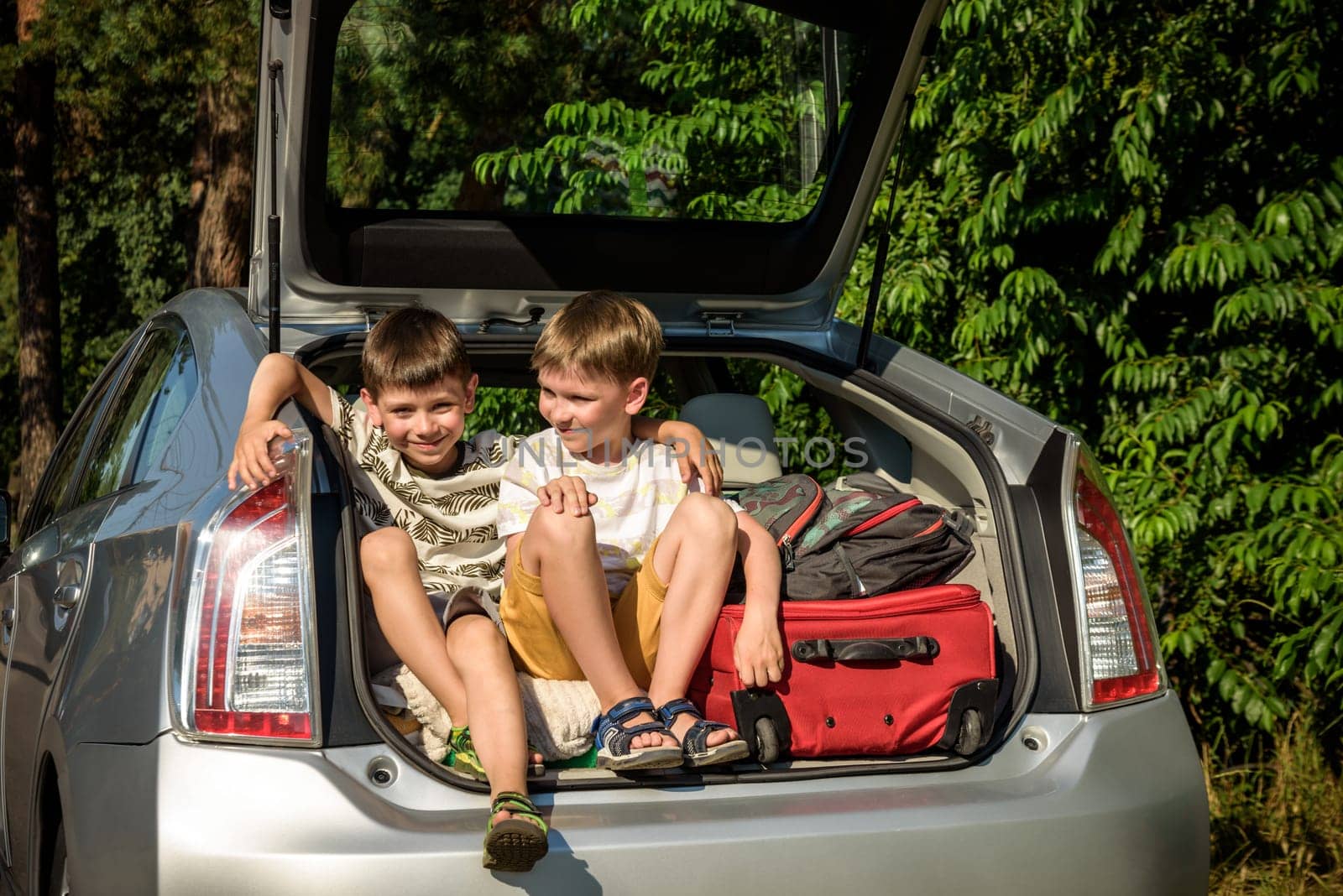 Two cute boys sitting in a car trunk before going on vacations with their parents. Two kids looking forward for a road trip or travel. Summer break at school. Family travel by car.