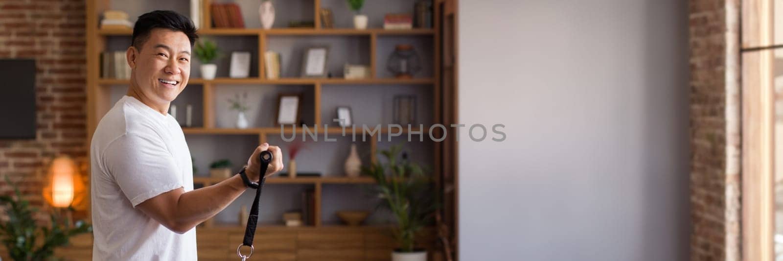 Home fitness concept. Happy korean mature man exercising using trx resistance bands and training in living room at home. Workout equipment and sporty lifestyle concept, copy space