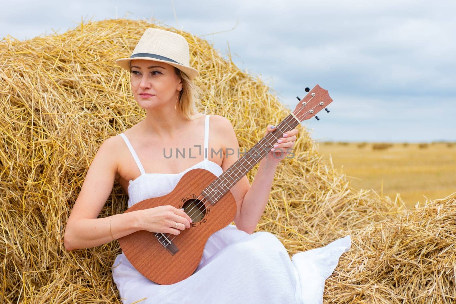 Young beautiful woman playing ukulele in haystack