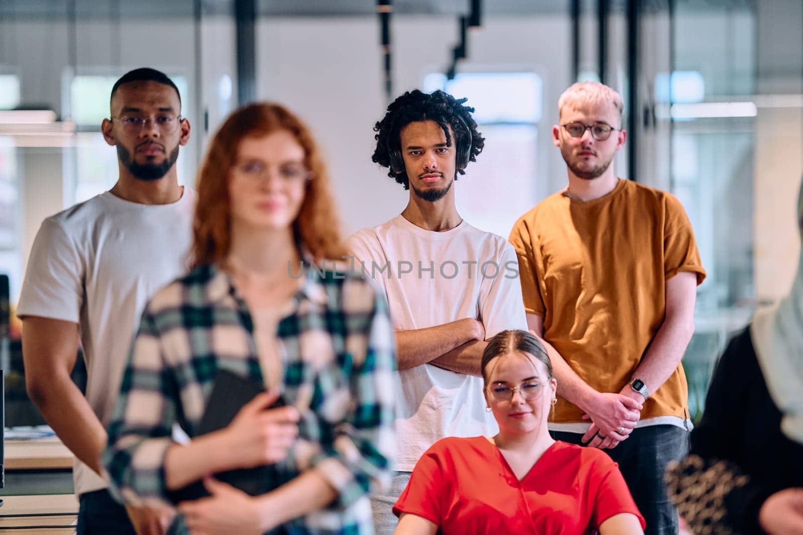 A diverse group of young business people walking a corridor in the glass-enclosed office of a modern startup, including a person in a wheelchair and a woman wearing a hijab by dotshock