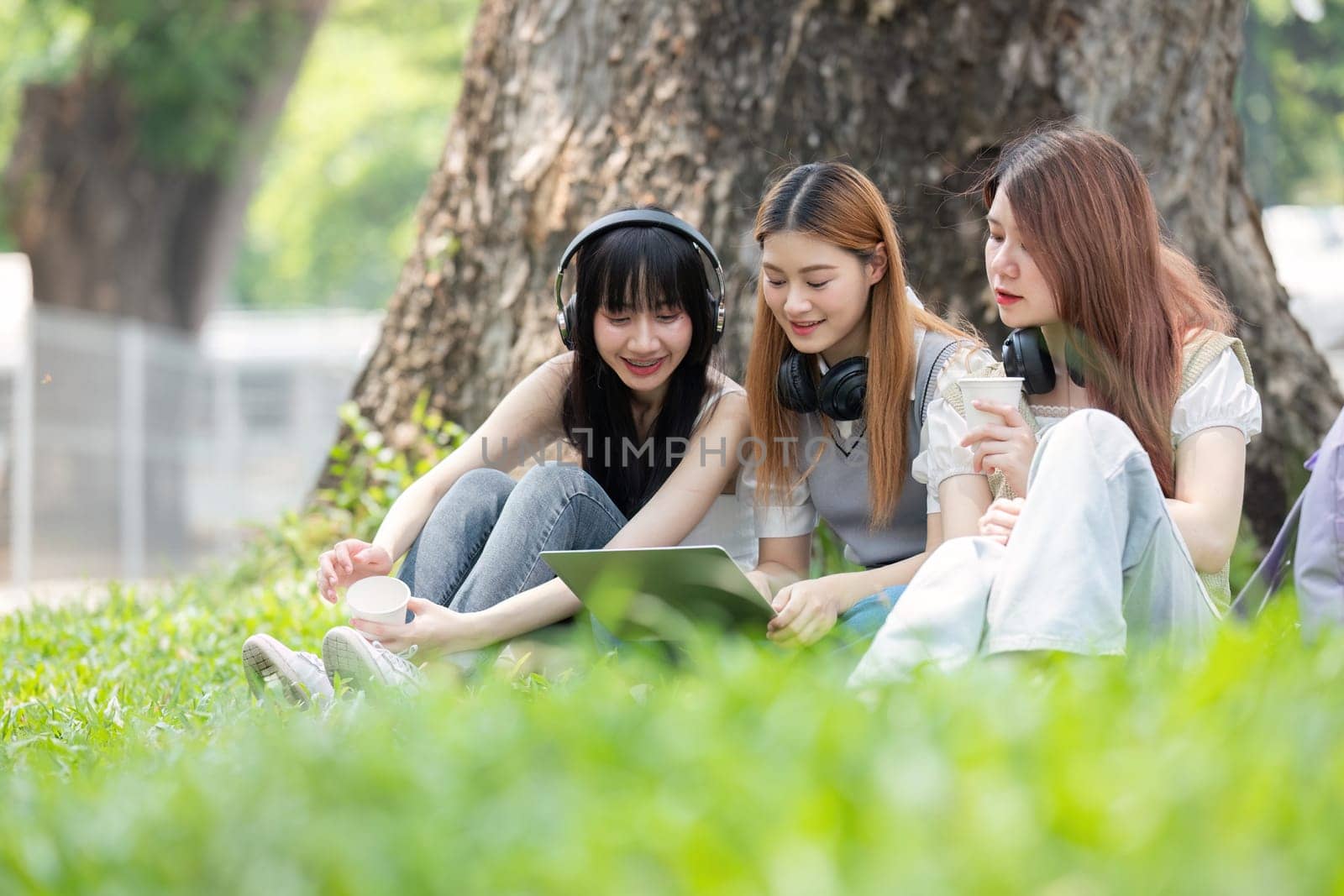 College student having discussion under tree on campus, preparing for exam, learning and reading books together.