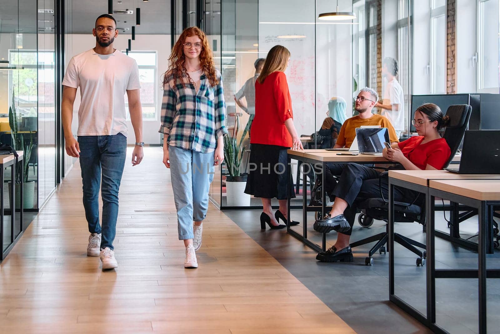 An African-American business colleague and his orange-haired female counterpart engage in collaborative discussion within a modern startup office, epitomizing diversity and teamwork in the entrepreneurial environment.