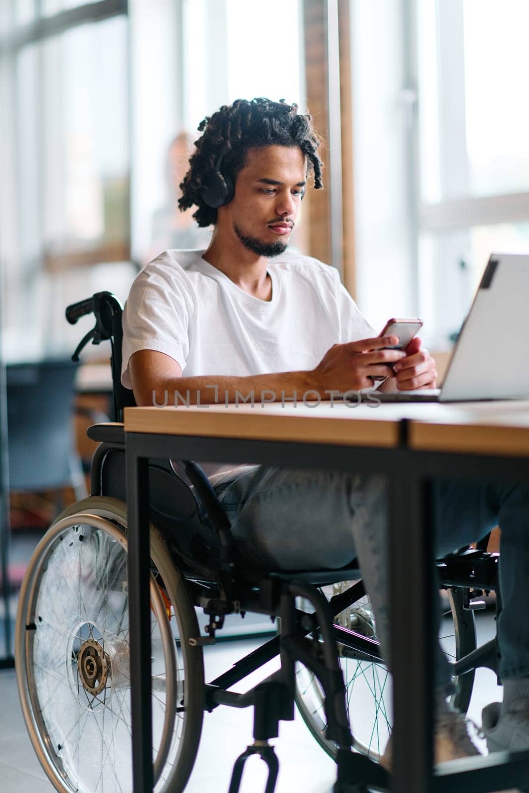An African American businessman in a wheelchair takes a work break, using his smartphone while seated in a modern business startup coworking center, reflecting both inclusion and technology integration