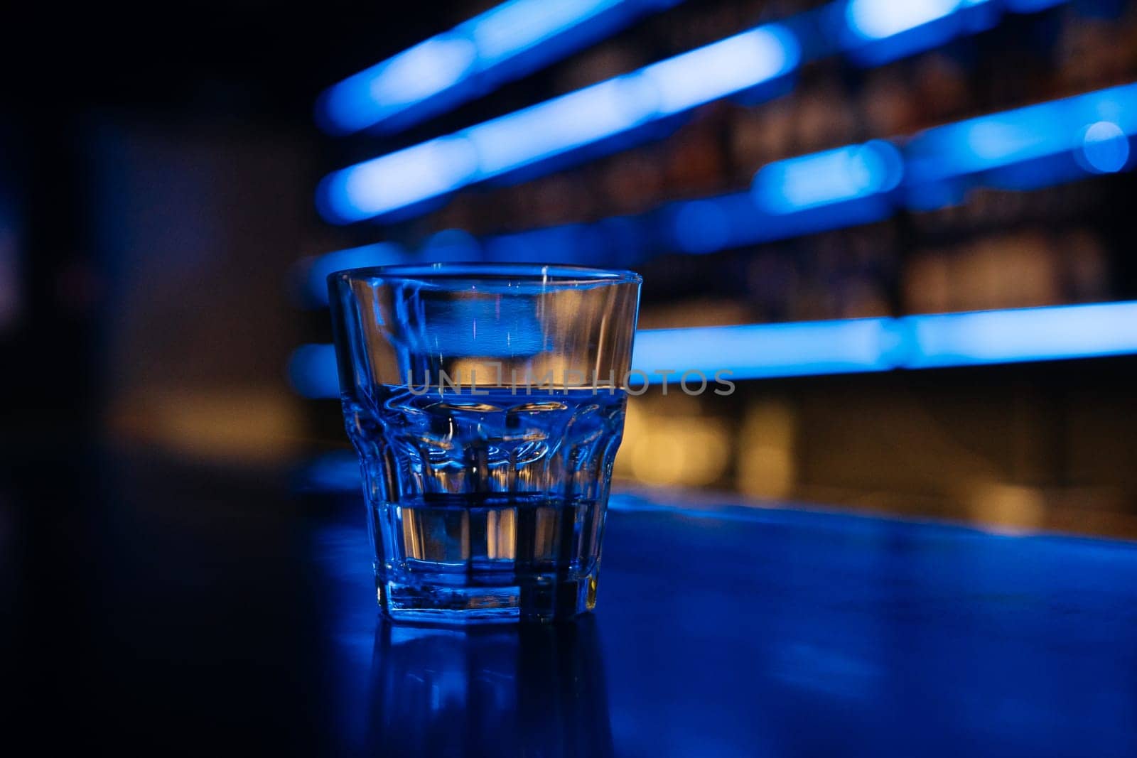 A glass of water sits on a bar counter. The bar is dimly lit, giving the scene a cozy and intimate atmosphere. by Matiunina