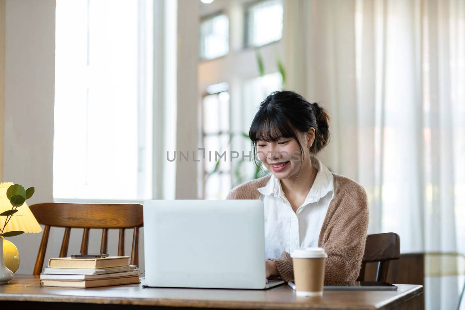 Asian students studying online talking together in an online chat meeting using laptops, studying online from home. by wichayada