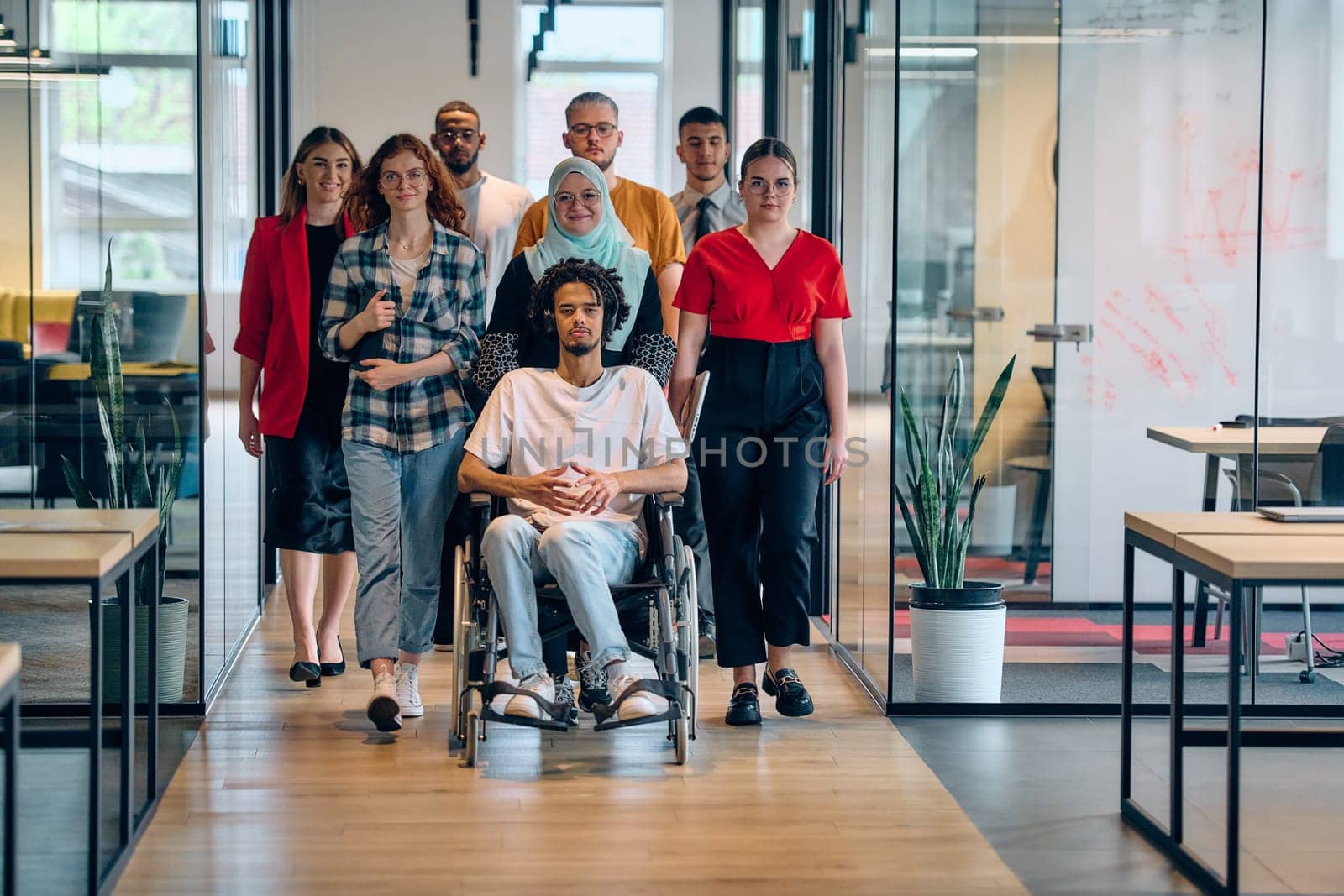 A diverse group of young business people congregates within a modern startup's glass-enclosed office, featuring inclusivity with a person in a wheelchair, an African American young man, and a hijab muslim woman . by dotshock