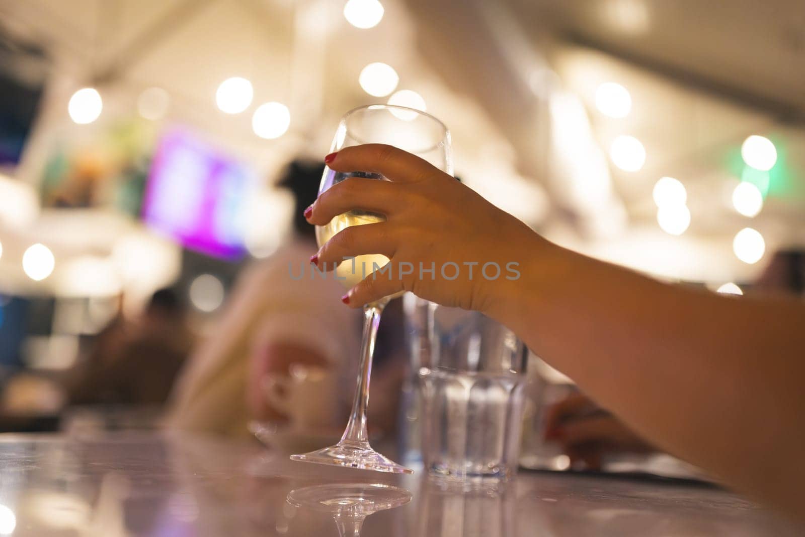 Woman's hand takes a glass ow white wine in restaurant, close up