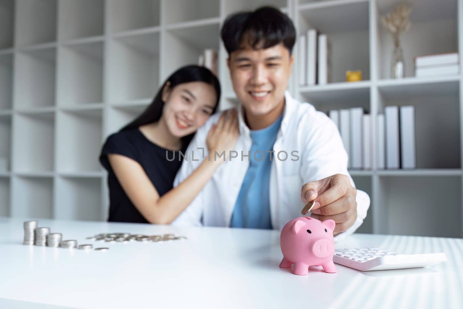 Young Asian couple putting coin to piggy bank for retirement together, Saving money concept.