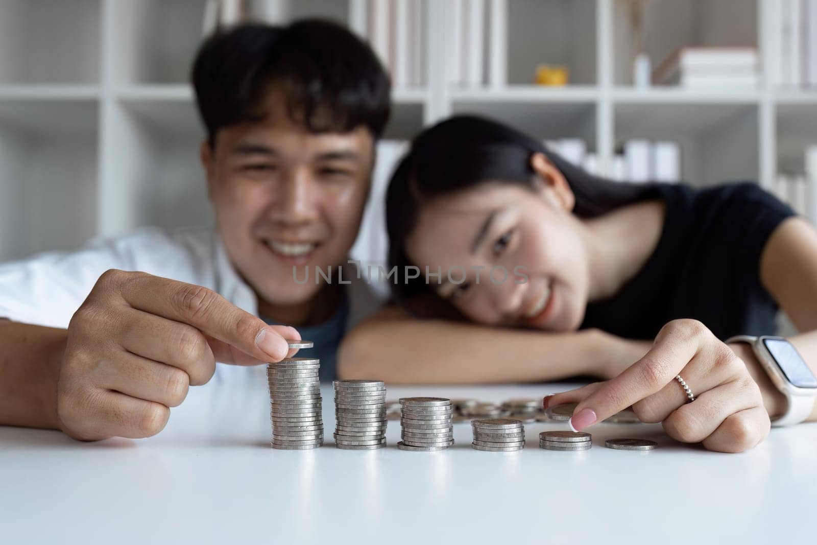 A man and woman are sitting at a table with a pile of coins in front of them by itchaznong