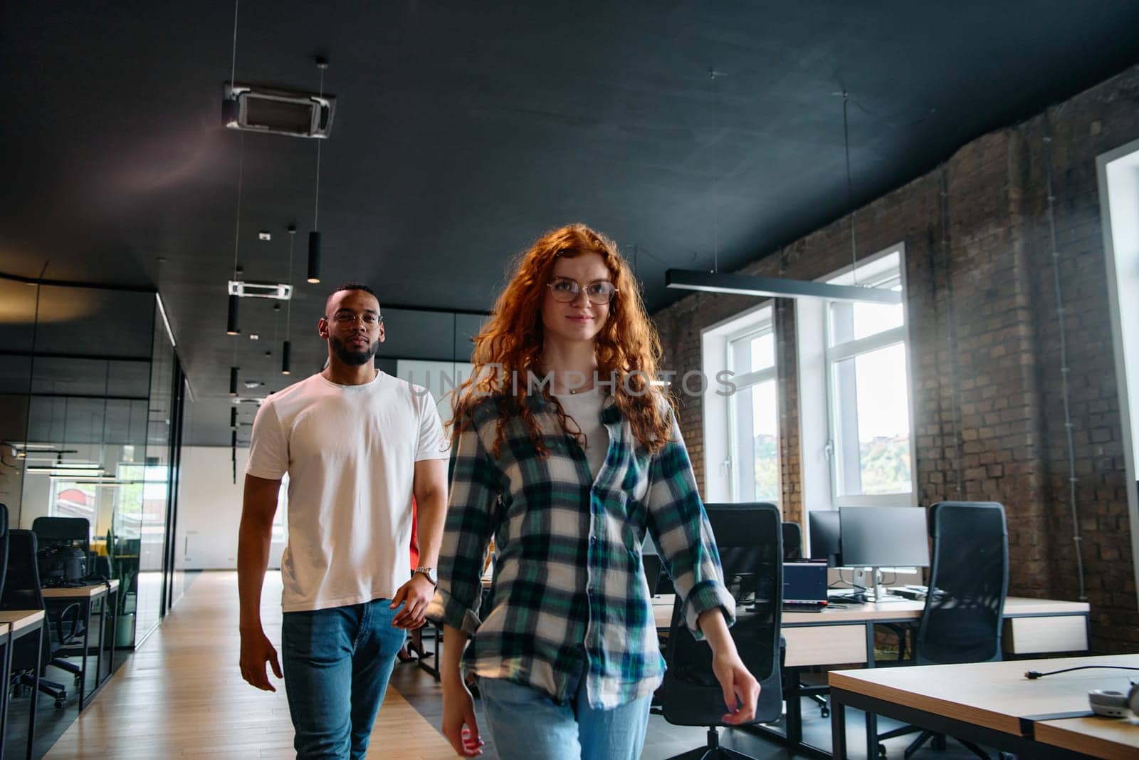 An African-American business colleague and his orange-haired female counterpart engage in collaborative discussion within a modern startup office, epitomizing diversity and teamwork in the entrepreneurial environment.