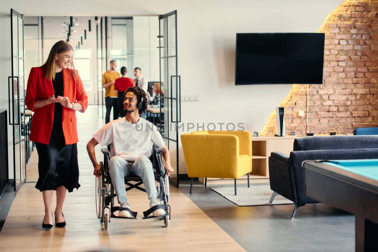 A diverse group of young professionals, including businesswomen and an African-American entrepreneur in a wheelchair, engage in collaborative discussion on various business projects in a modern startup office setting