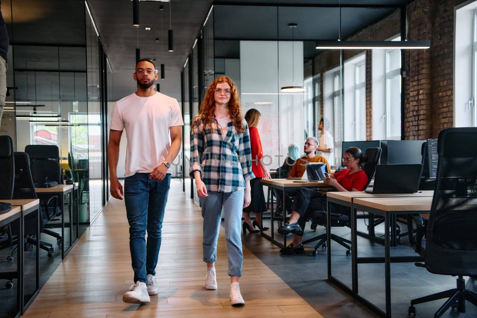 An African-American business colleague and his orange-haired female counterpart engage in collaborative discussion within a modern startup office, epitomizing diversity and teamwork in the entrepreneurial environment.